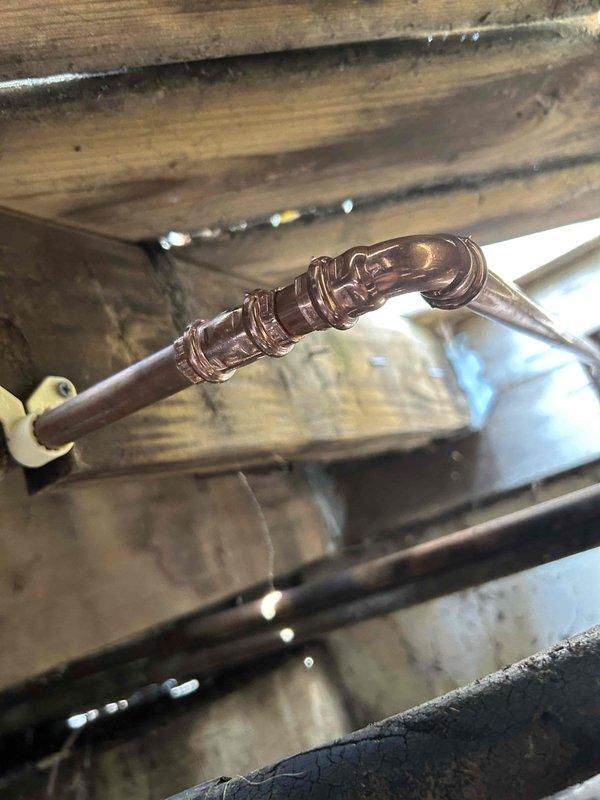 Responded to plumbing leak emergency involving a burst copper pipe located underneath deck structure. Upon inspection, identified significant split in copper water line running through crawl space beneath wooden decking, with visible moisture damage to surrounding wooden joists and beams. The pipe failure likely resulted from freeze damage during winter months. Successfully repaired the damaged section by cutting out the compromised copper pipe and installing a brazed coupling joint with proper soldering technique. Verified repair integrity and restored water service to the affected line.