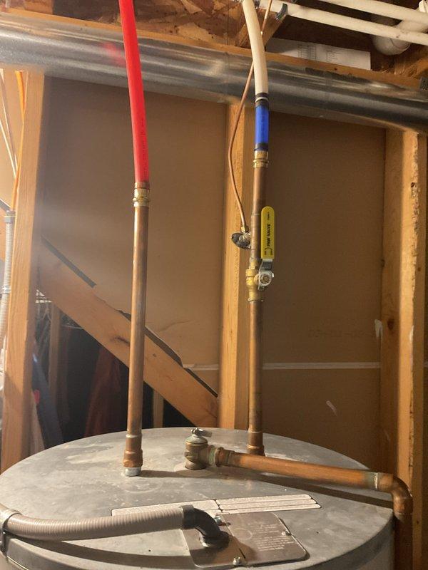 Provided estimate for water heater replacement in residential basement utility area. Assessed existing water heater installation with copper supply piping, brass fittings, and shut-off valve configuration. Documented current unit condition and plumbing connections including hot and cold water lines with insulated sleeves, T-junction piping arrangement, and flexible drain line. Photographed installation for quote preparation purposes.
