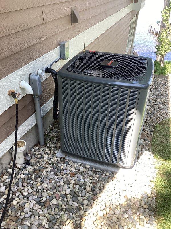 Complete air conditioning system replacement performed. Removed existing outdoor condensing unit and installed new heat pump system on concrete pad with decorative rock landscaping. Connected refrigerant lines with proper insulation, installed brass service valves, and performed system charging and diagnostics using manifold gauges. Mounted electrical disconnect box on exterior wall, ran electrical wiring and PVC condensate lines from building to new unit. System tested, verified proper operation, and left in full working condition.