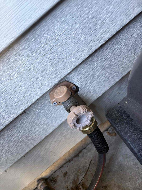 Responded to outdoor hose bib leak at residential property. Upon inspection, found active water leakage from brass outdoor spigot mounted on exterior vinyl siding. Assessed faucet assembly and connection points, documented existing conditions showing water discharge and weathered concrete foundation area. Identified source of leak and completed necessary repairs to stop water flow from the hose bib, restoring proper function to the outdoor water supply fixture.
