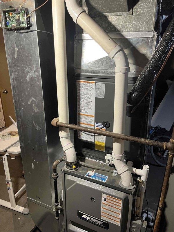 Completed full HVAC system replacement including outdoor condensing unit and indoor air handler. Removed existing equipment and installed new condenser on concrete pad with proper clearances from structure. Unit features protective top grille and side louvers for optimal airflow. Indoor installation includes new air handler positioned above furnace in mechanical room with integrated condensate drainage system using PVC piping, gas line connections, and properly sealed ductwork transitions. All electrical connections completed to code with disconnect box mounted on exterior wall. System tested for proper operation, refrigerant charge verified, and all safety controls confirmed functional.