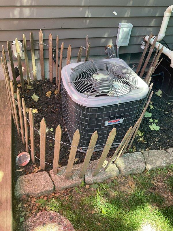 # Air Conditioning System No-Cooling Diagnosis and Service

Responded to service call for 16-year-old ICP air conditioning system with complete loss of cooling affecting entire residence. Upon arrival, performed comprehensive system evaluation of outdoor condensing unit located in side yard area.

Conducted visual inspection of condenser unit exterior, noting cylindrical design with mesh metal cage housing and protective fan grille. Verified unit positioning and clearances around equipment, observing adequate spacing from decorative fencing and proper drainage in mulched landscaping area.

Examined electrical connections and control wiring at condensing unit. Inspected refrigerant line sets and PVC condensate drainage piping running along exterior wall. Checked manufacturer's data plate for model specifications and refrigerant type to ensure proper service parameters.

Assessed condenser fan motor operation and compressor functionality. Evaluated capacitor condition and contactor perfo