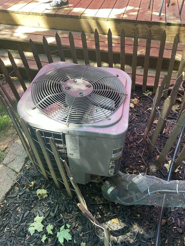 # Air Conditioning System No-Cooling Diagnosis and Service

Responded to service call for 16-year-old ICP air conditioning system with complete loss of cooling affecting entire residence. Upon arrival, performed comprehensive system evaluation of outdoor condensing unit located in side yard area.

Conducted visual inspection of condenser unit exterior, noting cylindrical design with mesh metal cage housing and protective fan grille. Verified unit positioning and clearances around equipment, observing adequate spacing from decorative fencing and proper drainage in mulched landscaping area.

Examined electrical connections and control wiring at condensing unit. Inspected refrigerant line sets and PVC condensate drainage piping running along exterior wall. Checked manufacturer's data plate for model specifications and refrigerant type to ensure proper service parameters.

Assessed condenser fan motor operation and compressor functionality. Evaluated capacitor condition and contactor perfo
