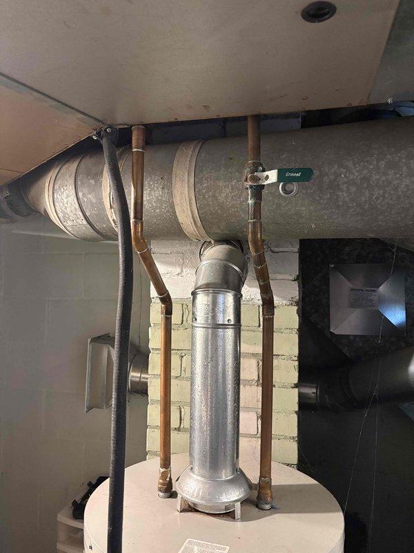 Responded to water leak complaint from 17-year-old ICP heating and cooling system. Upon inspection, found galvanized ductwork and copper piping assembly in basement utility area with visible water staining and mineral deposits on metal surfaces. Examined HVAC infrastructure including water heater connections, copper supply lines with oxidation, and galvanized metal ductwork mounted to masonry wall. Documented existing conditions with photos showing aged equipment, piping connections, and valve assemblies. Customer reported uncertainty about current heating and cooling functionality at time of service call.