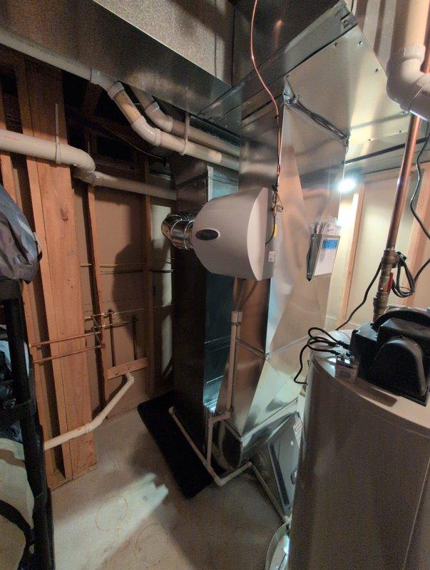 Completed full HVAC system installation including new furnace and air conditioning unit. Installed white furnace in basement utility area with proper ductwork connections, PVC condensate drainage lines, and electrical wiring per manufacturer specifications. Mounted outdoor condenser unit on concrete pad in exterior corner location between buildings, connected refrigerant lines to indoor unit, and verified proper system operation and refrigerant charge upon startup.