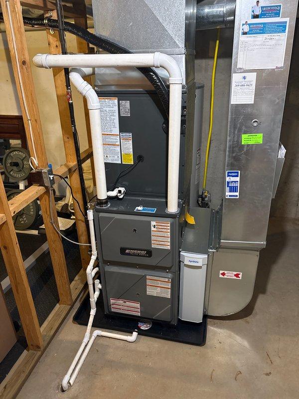 Completed full installation of new residential HVAC system including furnace and air conditioning unit in basement utility area. Installed dark gray furnace unit with proper PVC venting configuration including condensate drainage and exhaust piping with multiple 90-degree elbows. Mounted metallic air handler adjacent to furnace on concrete floor against unfinished wall. Connected refrigerant lines with proper insulation and installed brass service valves on exterior condensing unit. Verified refrigerant charge levels and documented system pressures (74/10/84 readings). Installed air distribution ductwork and metallic plenum box. Completed all electrical connections including conduit and wiring to both indoor and outdoor units. System tested and operational upon completion.