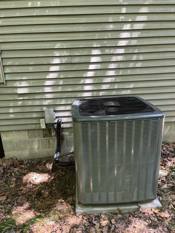 Completed full air conditioning system replacement at residential property. Removed existing outdoor condensing unit and installed new olive green condenser on existing concrete pad against exterior wall. Connected refrigerant lines and electrical conduit through vinyl siding to interior components. Mounted electrical disconnect box on exterior wall per code requirements. Verified all connections, tested system operation, and confirmed proper cooling performance upon startup.