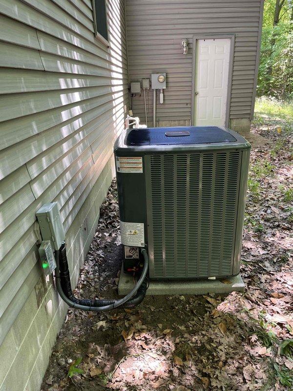 Completed full air conditioning system replacement at residential property. Removed existing outdoor condensing unit and installed new olive green condenser on existing concrete pad against exterior wall. Connected refrigerant lines and electrical conduit through vinyl siding to interior components. Mounted electrical disconnect box on exterior wall per code requirements. Verified all connections, tested system operation, and confirmed proper cooling performance upon startup.