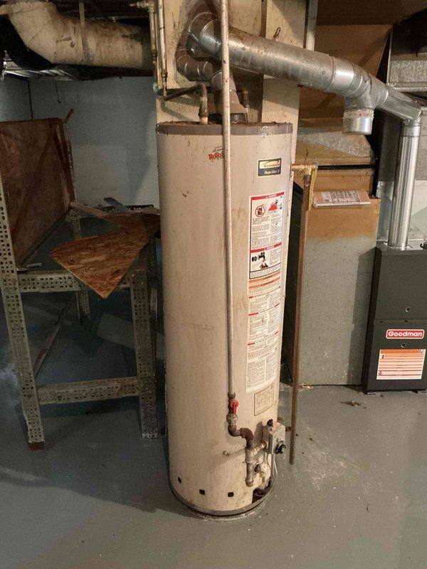 Conducted on-site assessment of existing water heater in basement utility area for replacement estimate. Inspected aging cylindrical water heater unit showing significant corrosion and rust at base connections, particularly where copper supply lines interface with the tank. Documented condition of existing plumbing connections including copper and galvanized steel piping, vent stack configuration, and proximity to electrical panel. Evaluated basement mechanical room layout, ceiling clearances with exposed floor joists, and access requirements for equipment removal and installation. Photographed current water heater specifications, warning labels, and surrounding HVAC equipment to determine appropriate replacement unit sizing and compatibility with existing infrastructure.