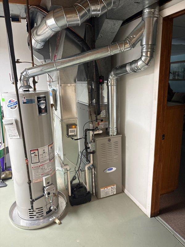 Completed full installation of new furnace and air conditioning system in residential basement utility room. Installed beige furnace unit with proper ventilation panels and gray AC air handler equipped with flammable refrigerant safety labels and warnings. Connected all necessary ductwork including metallic distribution system with proper elbow joints and fastening bands throughout ceiling area. Installed flexible corrugated ducting and copper refrigerant lines to air handler unit. Verified all equipment clearances meet code requirements and ensured proper positioning adjacent to existing water heater. System tested and operational upon completion.