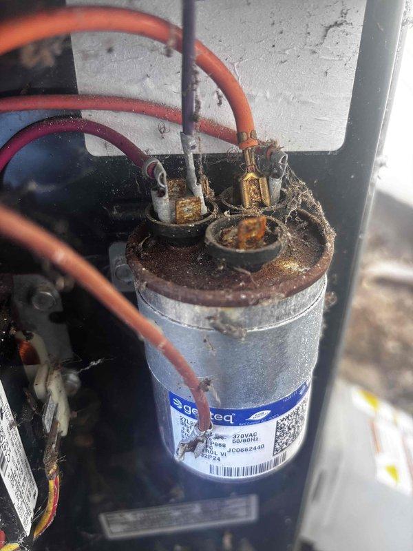 # AC Annual Cooling Maintenance Visit

Performed comprehensive annual cooling system maintenance on a 10+ year old air conditioning unit. Upon inspection, discovered severe corrosion and rust accumulation on the capacitor terminals and electrical connections, indicating prolonged moisture exposure and potential component failure risk. The capacitor showed significant deterioration at the top terminal area with heavy oxidation affecting wire connection points.

Found substantial debris accumulation inside the unit, including dried leaves, twigs, and organic matter that had collected around wire entry points and throughout the interior compartment. This debris posed risks for airflow restriction, electrical hazards, and potential pest intrusion. Cleaned all accessible areas to remove organic materials and restore proper equipment clearances.

Inspected all electrical connections and wiring despite corrosion present on capacitor terminals. Multiple wires including orange, red, and gray co