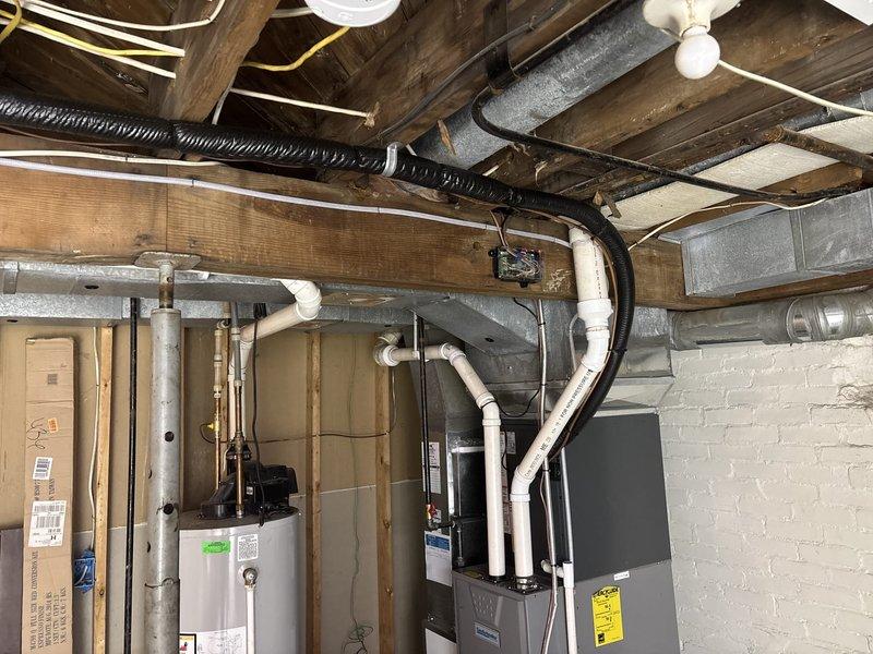 Responded to water leak in basement mechanical room. Upon inspection, identified active leak originating from PVC plumbing connections near ceiling joists above HVAC equipment and water heater. Documented existing conditions with photos showing water damage potential to electrical components, including outlet box and transformer mounted on wall below affected piping. Traced leak source to compromised joint in drainage system running along ceiling beams. Repaired faulty connection, secured all loose PVC fittings, and verified proper slope of horizontal drain lines. Tested system under full flow conditions to confirm leak resolution. Advised monitoring area for any residual moisture and recommended evaluation of electrical components for water exposure damage.