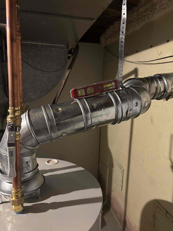 Corrected water heater venting system to meet code requirements by adjusting the horizontal vent pipe slope using proper support methods. The flexible metal duct was repositioned and secured with appropriate hangers to ensure proper drainage and prevent condensation accumulation, resolving the inspection violation for improper venting slope.