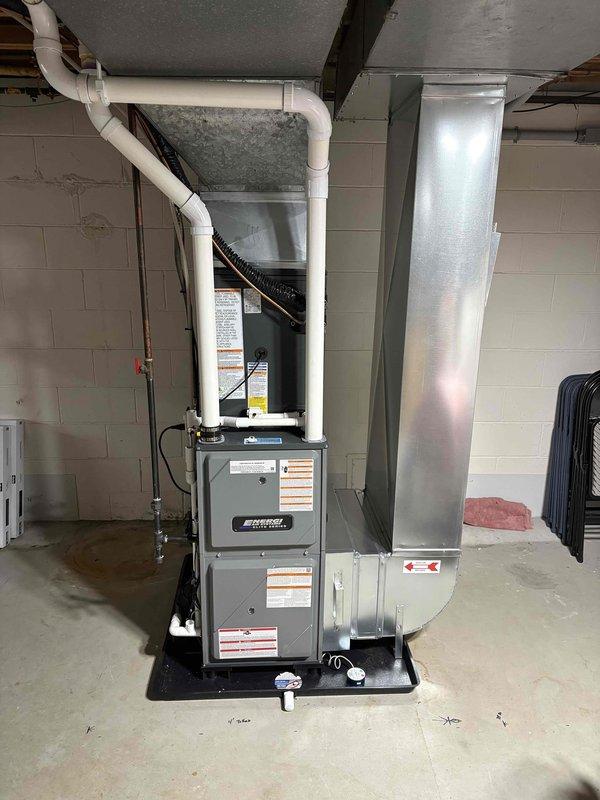 Completed full installation of new furnace and air conditioning system in basement utility area. Installed furnace unit on protective drain pan with proper clearances, connected white PVC venting system with appropriate routing to exterior, and integrated black flexible ductwork connections. Established galvanized sheet metal plenum connections to existing ductwork distribution system, verified all electrical connections, and ensured proper condensate drainage. System tested and operational upon completion.
