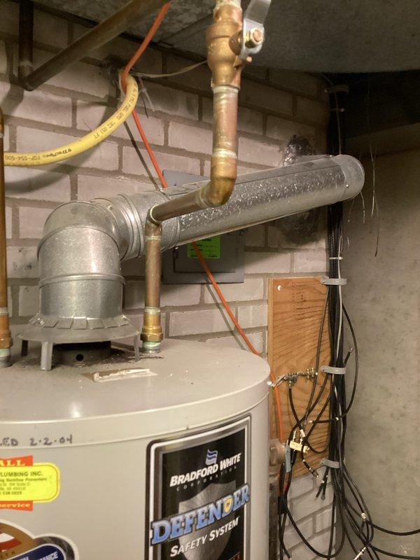 Conducted on-site evaluation of existing Bradford White Defender water heater system installed in 2004 to provide estimate options for both tankless and traditional tank-style replacement units. Documented current installation configuration including copper supply piping, venting system, gas connections, and observed condensation on horizontal piping indicating potential efficiency concerns with aging equipment.