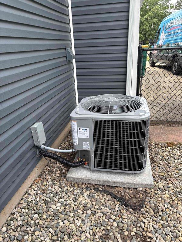 Completed full air conditioning system replacement including outdoor condenser unit installation on concrete pad with river rock landscaping. Unit was properly positioned against building exterior with electrical conduit and refrigerant lines connected from wall-mounted junction box. System was charged and pressure-tested using manifold gauges to verify proper refrigerant levels and operating parameters across all zones.