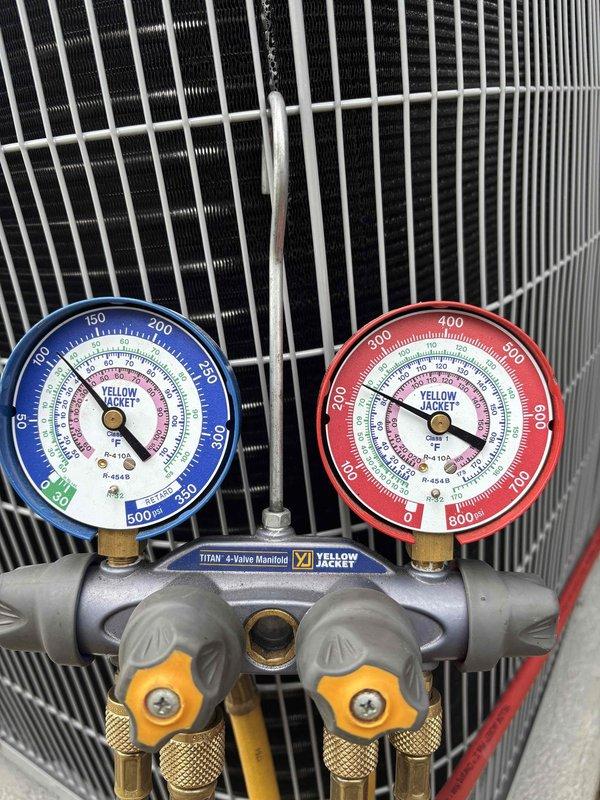 Completed full air conditioning system replacement including outdoor condenser unit installation on concrete pad with river rock landscaping. Unit was properly positioned against building exterior with electrical conduit and refrigerant lines connected from wall-mounted junction box. System was charged and pressure-tested using manifold gauges to verify proper refrigerant levels and operating parameters across all zones.