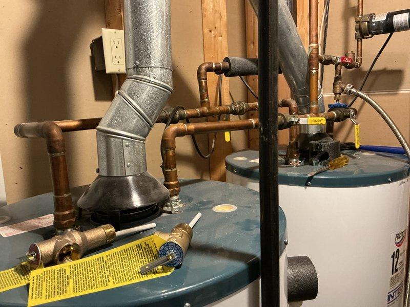 Completed estimate for replacement of two residential water heaters in utility room, with one unit actively leaking. Assessed existing installation including dual water heater configuration with interconnected copper piping, brass valves, galvanized venting system, and associated gas lines. Documented current plumbing infrastructure, vent routing through ceiling joists, and electrical connections to provide accurate replacement specifications and scope of work.