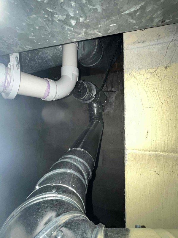 # IAQ Miscellaneous Service - B-Vent Modification

Responded to a no-charge service call to address B-vent configuration issues in the mechanical space. Upon inspection, identified improper temporary sealing on a 4" B-vent tee assembly with tape that required removal and proper termination.

Evaluated the existing vent configuration, which included galvanized metal ductwork with 90-degree elbows showing moisture accumulation, white PVC drainage piping, and black flexible insulated ductwork in the crawlspace area. Determined the optimal solution for proper venting compliance.

Removed temporary tape sealing from the 4" B-vent tee and installed appropriate cap to ensure proper termination. Alternatively assessed the option to remove the existing tee entirely and install a 5" to 4" single-wall reducer with a 4" 90-degree single-wall elbow for improved venting performance.

Verified all connections were secure and properly sealed according to manufacturer specifications and local code requ