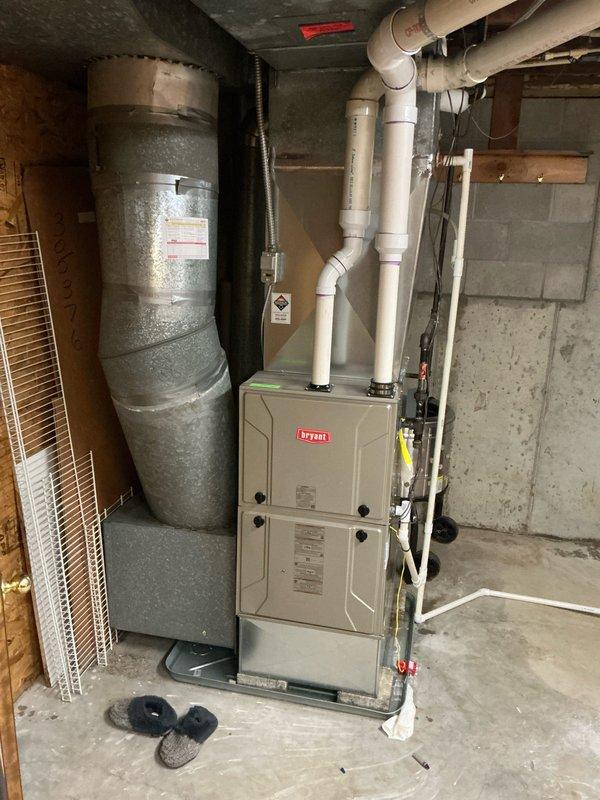 Responded to service call for non-operational air conditioning system at 9 AM. Conducted comprehensive assessment of residential HVAC installation located in basement mechanical room. Inspected Bryant furnace unit, metallic air handler with silver exterior finish, associated ductwork including large gray flexible ducts, white PVC condensate drain lines, and cylindrical expansion tank. Documented existing equipment configuration with photographs showing complete system layout, including exposed wiring, copper piping, galvanized ductwork with insulation, and all mechanical connections. Evaluated overall system condition and operational status to prepare detailed estimate for necessary repairs or replacement.