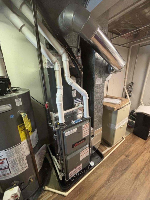 Completed full furnace installation in residential basement mechanical room. Installed new Amana furnace unit on wooden platform with proper PVC venting and condensate drainage piping routed vertically. Connected metal ductwork to existing system through ceiling joists, integrated with air handler cabinet, and ensured all manufacturer specifications and safety requirements were met for residential heating system operation.