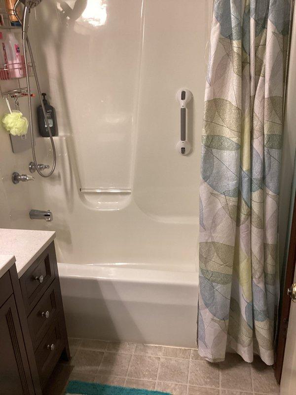 Conducted on-site assessment of existing bathtub-shower combination unit for conversion to walk-in shower installation. Documented current bathroom configuration including white fiberglass tub surround, chrome fixtures, grab bar placement, and vanity positioning. Photographed existing plumbing connections, shower valve assembly, and tub drain location to prepare specifications for tub removal and barrier-free shower replacement.