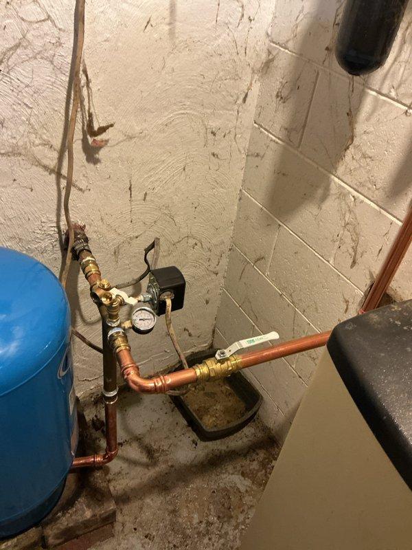 Installed new blue pressure tank in utility area with associated tank tee fitting and plumbing connections. Connected copper piping with brass fittings and shut-off valves to integrate pressure tank into existing water system. Installed pressure control device with gauge to monitor system operation and ensure proper water pressure regulation throughout the residence.