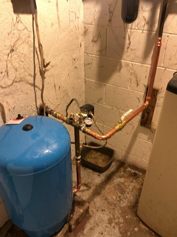 Installed new blue pressure tank in utility area with associated tank tee fitting and plumbing connections. Connected copper piping with brass fittings and shut-off valves to integrate pressure tank into existing water system. Installed pressure control device with gauge to monitor system operation and ensure proper water pressure regulation throughout the residence.