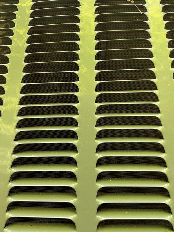 Completed annual cooling maintenance on EnergiAir system with 2023 condenser model. Inspected outdoor unit ventilation louvers and found them functioning properly with minor surface wear on yellow-green painted housing. Documented significant moisture condensation buildup on upper equipment surfaces and extensive rust corrosion on horizontal metal brackets and mounting components, indicating prolonged exposure to moisture and potential drainage issues. Recommended monitoring unit for continued corrosion progression and consideration of rust remediation to prevent structural deterioration of affected components.