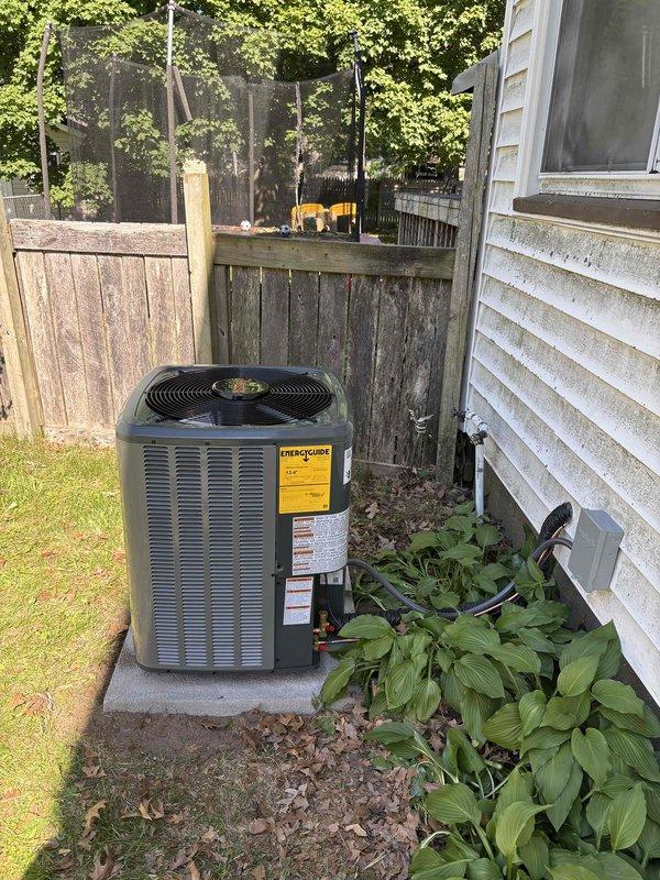 Completed full HVAC system replacement including outdoor condensing unit and indoor air handler with furnace. Installed new dark gray condenser on existing concrete pad with proper electrical disconnect, refrigerant lines, and drainage connections. Mounted new air handler above existing furnace in basement mechanical room, connected copper refrigerant lines, PVC condensate drain, and integrated with existing ductwork using flexible transitions. System tested and verified operational with all safety labels applied per manufacturer specifications.