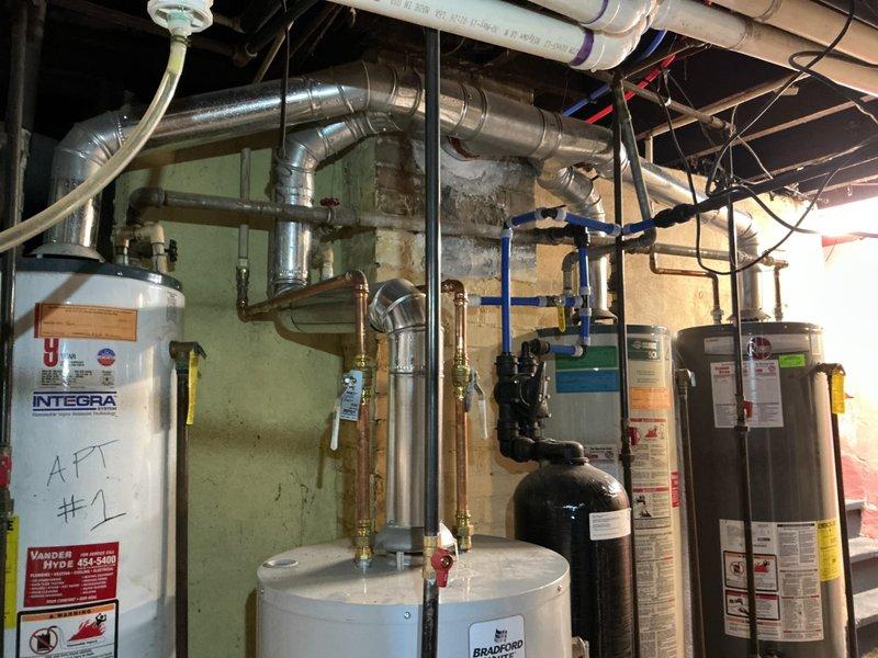 Completed rental inspection of basement mechanical room containing multiple water heaters and furnace system. Documented equipment conditions, verified proper installation of HVAC ductwork, plumbing connections with copper piping and blue-handled valves, and confirmed presence of city plumbing inspection approval stickers on units. Photographed all equipment including Bradford White and Integra branded water heaters for rental property compliance records.