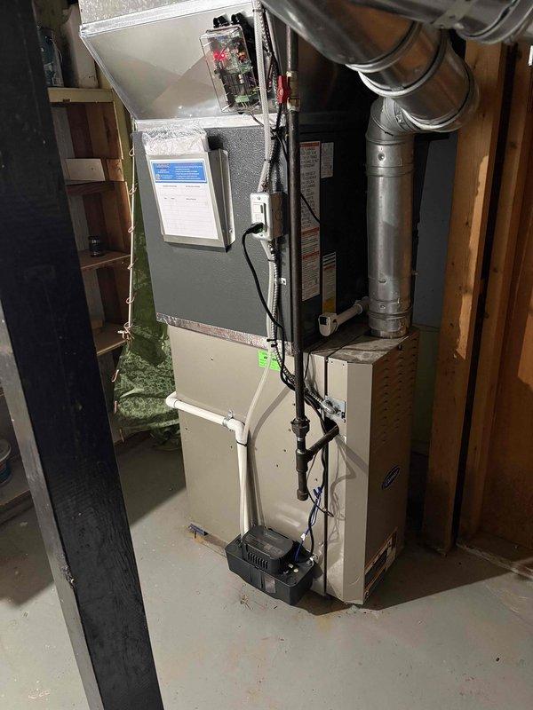 Completed full HVAC system replacement including outdoor condensing unit and indoor air handler. Removed existing equipment and installed new silver/gray condenser unit on concrete pad in side yard with proper refrigerant line connections and electrical disconnect. Installed new furnace/air handler in basement utility area with associated ductwork connections and electrical wiring. All refrigerant lines, electrical conduit, and drainage properly routed and secured. System tested and verified operational upon completion.