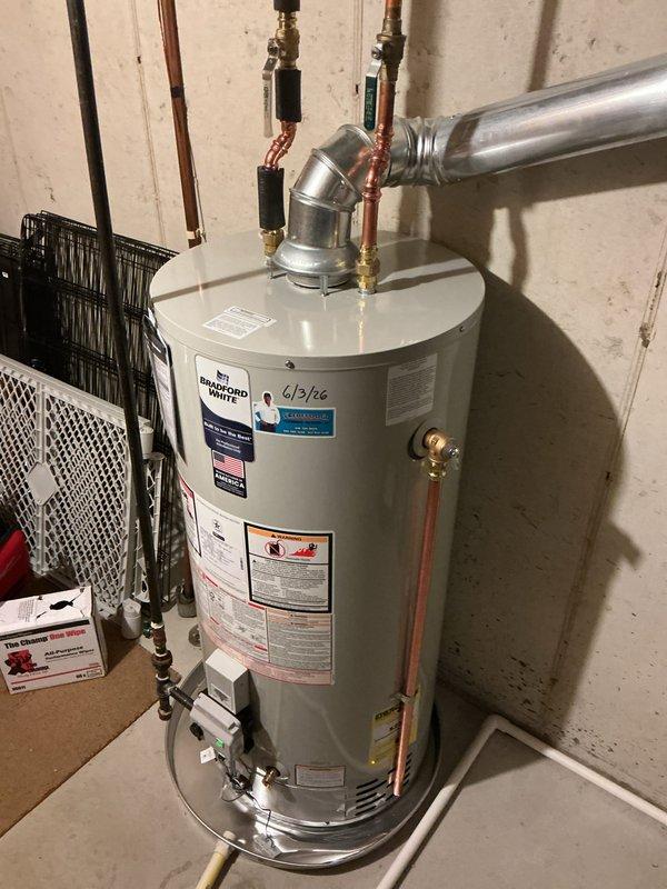 Completed installation of a 40-gallon Bradford White natural gas water heater in residential utility room. Unit was properly positioned, connected to existing copper water supply lines with brass fittings and compression valves, and vented with metallic ductwork including elbow joint for proper exhaust routing. All plumbing connections, gas line hookups, temperature and pressure relief valve, and safety controls were installed per manufacturer specifications and local code requirements.