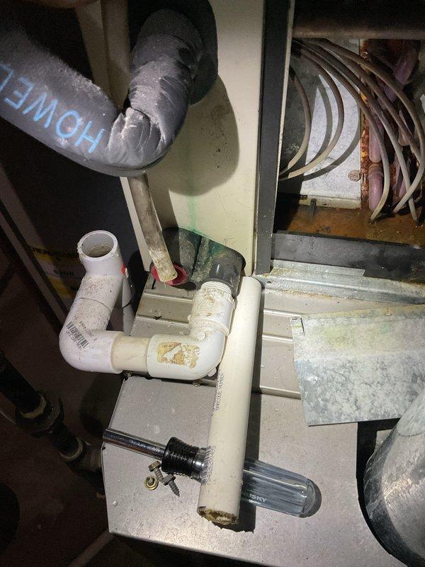 Responded to water leak complaint on 20+ year old Bryant furnace. Upon inspection, found condensate drain system with visible mineral deposits and staining on PVC drain lines. Examined condensate pump assembly with float switch and drainage piping configuration. Verified refrigerant lines and flexible ductwork connections. Documented existing condensate management system showing signs of age-related wear and mineral buildup on drain components.