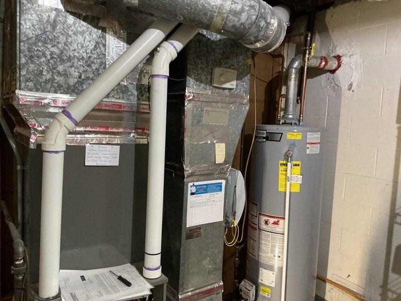 Completed comprehensive rental inspection of 7-year-old Rheem HVAC system and water heating equipment in basement utility area. Documented all mechanical systems including green-painted furnace unit with PVC condensate drainage configuration, gray water heater with proper labeling, copper supply lines, and flexible ductwork routing. Photographed equipment specifications, piping connections with purple primer marks at joints, brass valve assemblies, and PVC pipe distribution system labeled for room identification throughout the property.