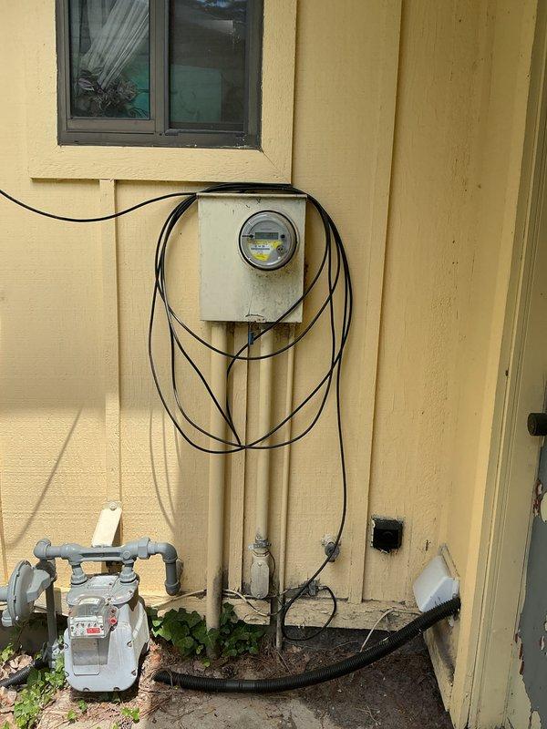 Responded to electrical service call regarding breaker box with no voltage to outside unit and intermittent smoking from breaker. Inspected main electrical panel located in basement utility area and exterior meter installation on side of residence. Documented existing conditions showing multiple circuit breakers, wiring configurations running from panel to ceiling space, and exterior electrical service entrance with meter enclosure and associated conduit connections. Provided estimate for necessary electrical repairs to resolve voltage issue and eliminate safety hazard from smoking breaker.