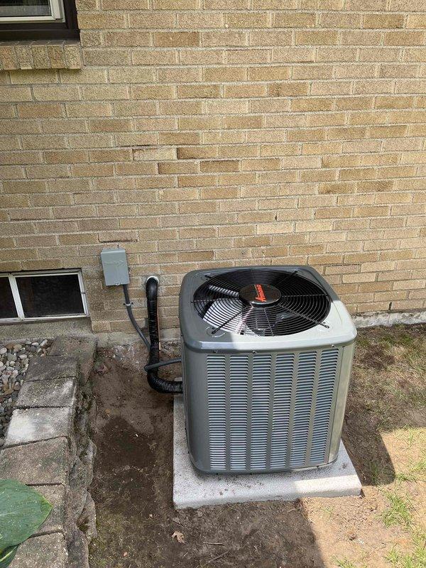 Completed full HVAC system installation including new furnace and air conditioning unit. Interior furnace installed in basement utility area with all internal components properly connected, including copper refrigerant lines, electrical wiring, and motor assemblies integrated with existing ductwork system. Exterior condenser unit positioned on concrete pad against building exterior with refrigerant lines and electrical connections routed through wall penetration, condensate drain line secured along exterior wall to electrical disconnect box. Both units tested and verified operational upon completion of installation.