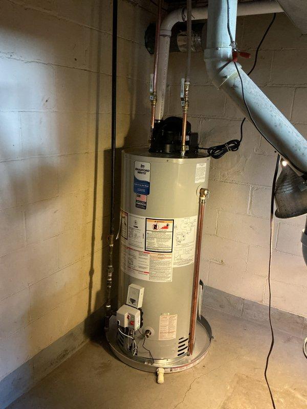 Completed installation of a 40-gallon power vent water heater in residential basement utility area. Unit was properly positioned on concrete floor against cinder block wall, with all copper supply lines, brass shut-off valves, electrical connections, and venting ductwork installed per manufacturer specifications and local code requirements.
