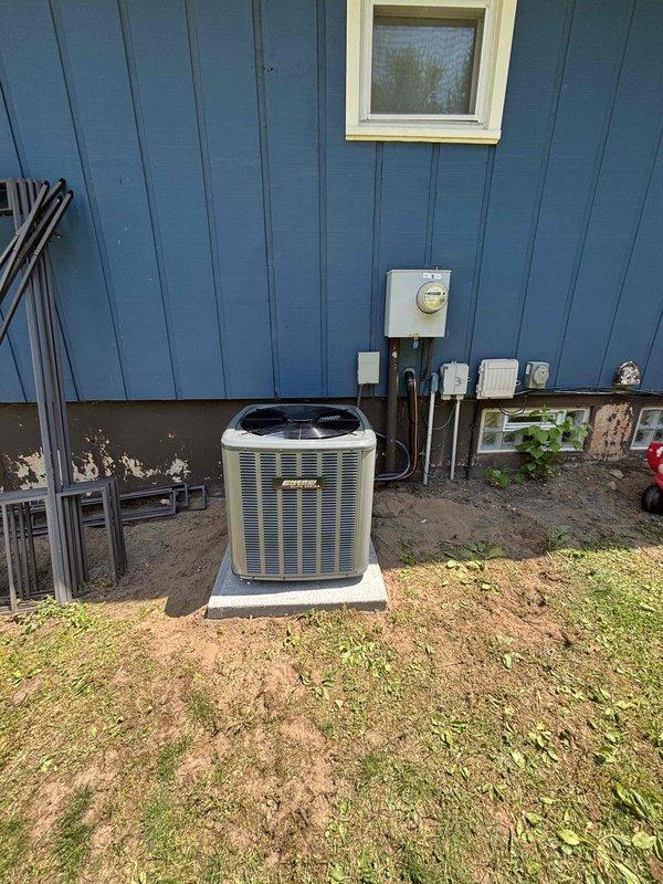 Successfully completed full air conditioning system replacement at residential property with blue vertical siding. Removed existing AC condenser unit and installed new gray condensing unit on existing concrete pad. Connected refrigerant lines with proper black insulation wrapping and secured all copper line sets along exterior wall to indoor air handler. Completed all electrical connections to existing meter base and verified proper voltage supply. Tested system operation including compressor startup, fan motor function, and refrigerant pressures to manufacturer specifications. All components operational and system cooling effectively upon completion.