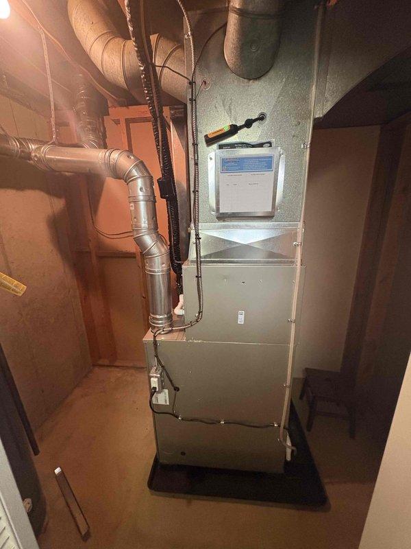 Completed full HVAC system installation including new furnace and air conditioning condenser unit. Furnace installed in interior utility space with proper ductwork connections, metallic supply plenum, and digital thermostat control panel mounted on unit. AC condenser positioned on concrete pad against exterior wall with appropriate clearances, connected to indoor system via refrigerant lines and electrical service. All ductwork properly sealed and secured, condensate drainage configured, and system tested for proper operation. Unit confirmed operational with correct airflow, temperature differential, and refrigerant charge verified within manufacturer specifications.