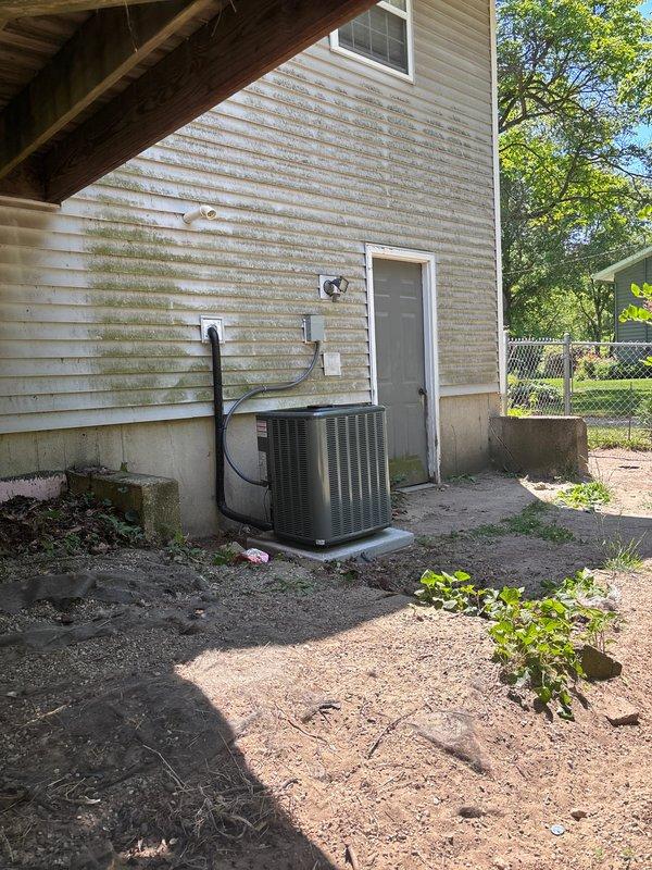 Completed full air conditioning system replacement at residential property. Removed existing outdoor condensing unit and installed new AC condenser on concrete pad against exterior wall with proper refrigerant line connections routed up exterior siding to indoor air handler. Connected system to existing furnace and ductwork in basement utility area, verified proper electrical connections, charged system to manufacturer specifications, and tested all components for proper operation and airflow.