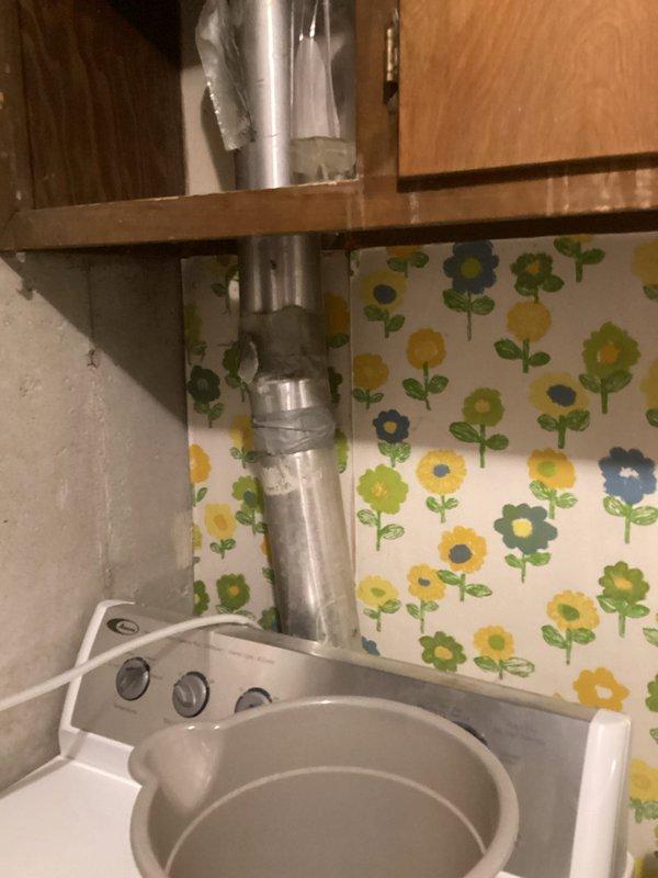 Relocated gas lines and replaced dryer vent ducting in laundry utility area. Installed new metallic flexible vent duct running vertically through wooden shelf structure behind washing machine, ensuring proper ventilation and code compliance. Gas line relocation completed to accommodate revised laundry room configuration.