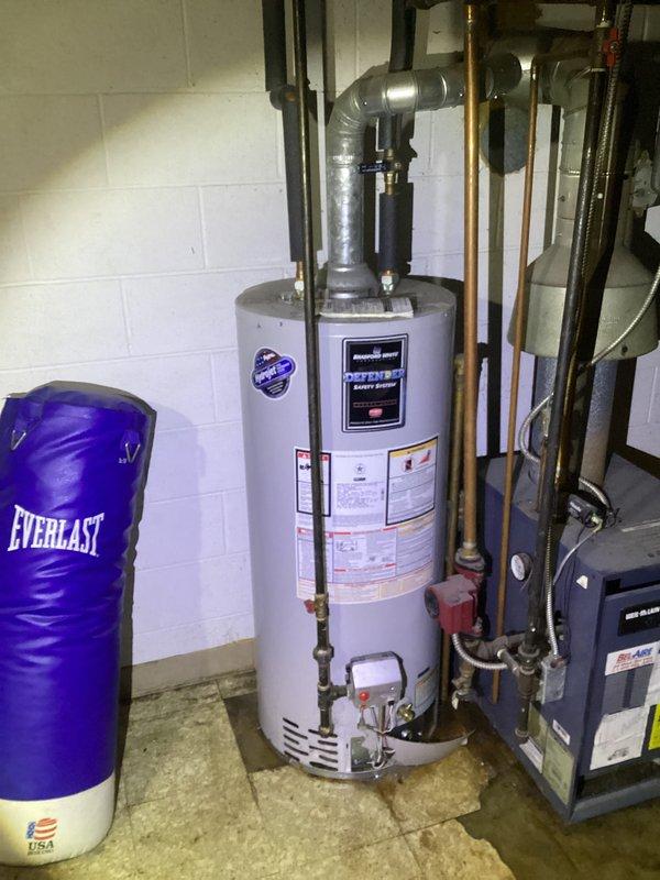 Responded to service call for water heater leaking with no hot water production. Upon arrival, inspected existing water heater unit over 10 years old showing signs of tank failure and active water leakage at base. Documented condition of failed unit and surrounding plumbing connections including copper supply lines and metallic ductwork. Confirmed unit was beyond economical repair due to age and extent of deterioration. Photographed installation area showing water heater positioned in basement utility room alongside HVAC equipment with standard plumbing configuration.