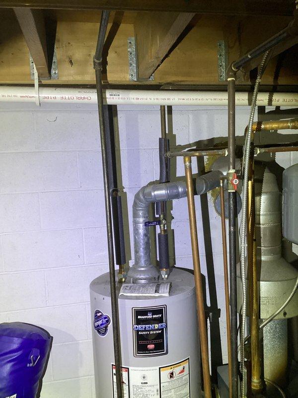 Responded to service call for water heater leaking with no hot water production. Upon arrival, inspected existing water heater unit over 10 years old showing signs of tank failure and active water leakage at base. Documented condition of failed unit and surrounding plumbing connections including copper supply lines and metallic ductwork. Confirmed unit was beyond economical repair due to age and extent of deterioration. Photographed installation area showing water heater positioned in basement utility room alongside HVAC equipment with standard plumbing configuration.