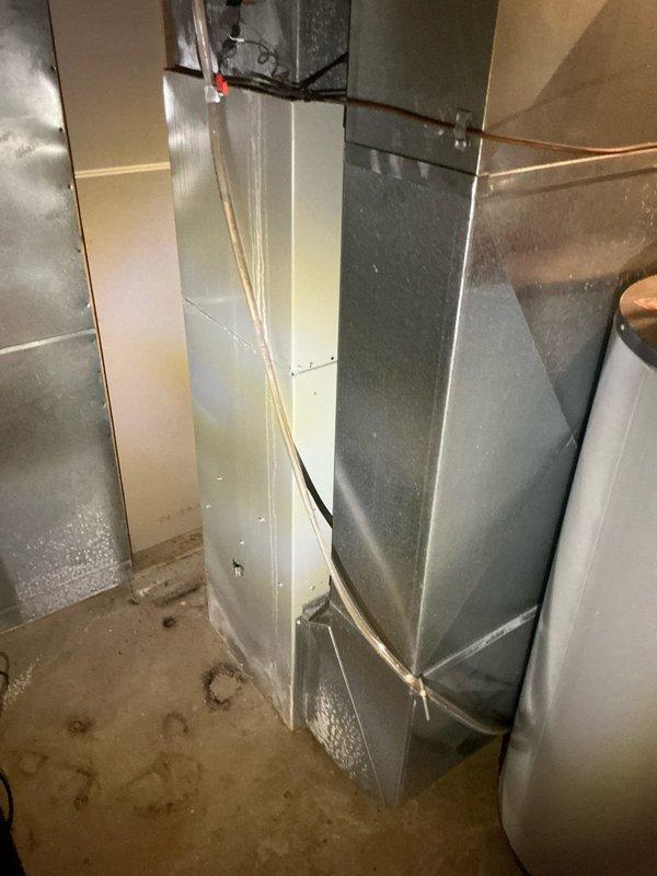 Performed proactive sales estimate for replacement of 25-year-old residential air conditioning system in condo unit. Existing unit currently operational with no reported performance issues. Inspected HVAC equipment and ductwork in basement mechanical area, noting condensation present on galvanized metal ductwork surfaces and moisture staining on concrete floor beneath system. Evaluated exterior condenser unit located in narrow side yard area between buildings on gravel and mulch surface. Documented existing system configuration and conditions through photographic assessment to provide accurate replacement recommendations for aging equipment nearing end of expected service life.