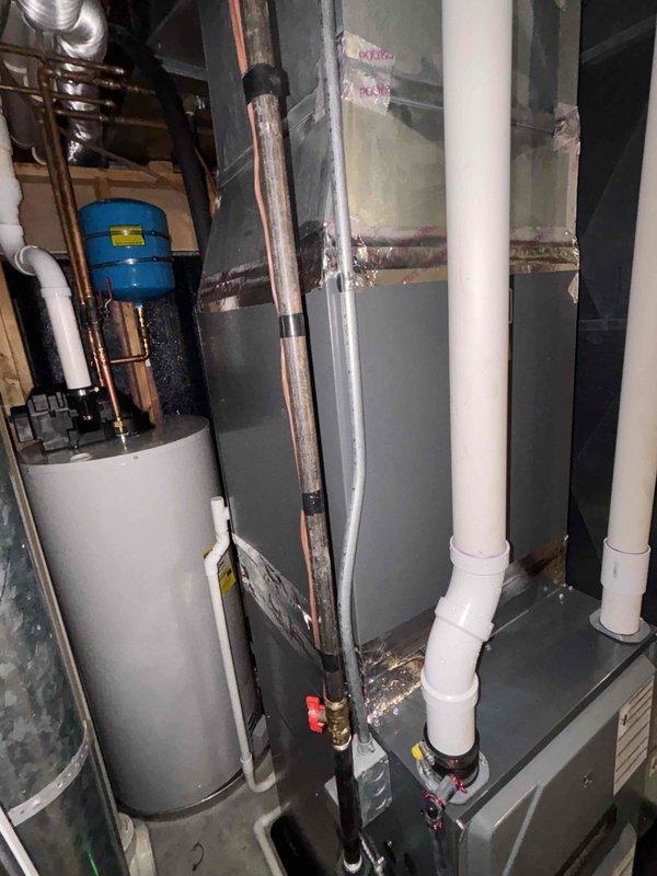 Completed installation of water softener system, water heater, and toilet replacement in residential mechanical room. Installed new water heater with proper copper piping connections, mounted blue expansion tank above unit, and integrated red-handled isolation valves for system control. Routed copper supply lines throughout utility space, connecting water softener to main plumbing system while maintaining proper clearances around existing HVAC equipment and air handling units. Installed white PVC drainage and vent piping for proper system discharge, ensuring all connections meet code requirements in the confined workspace.