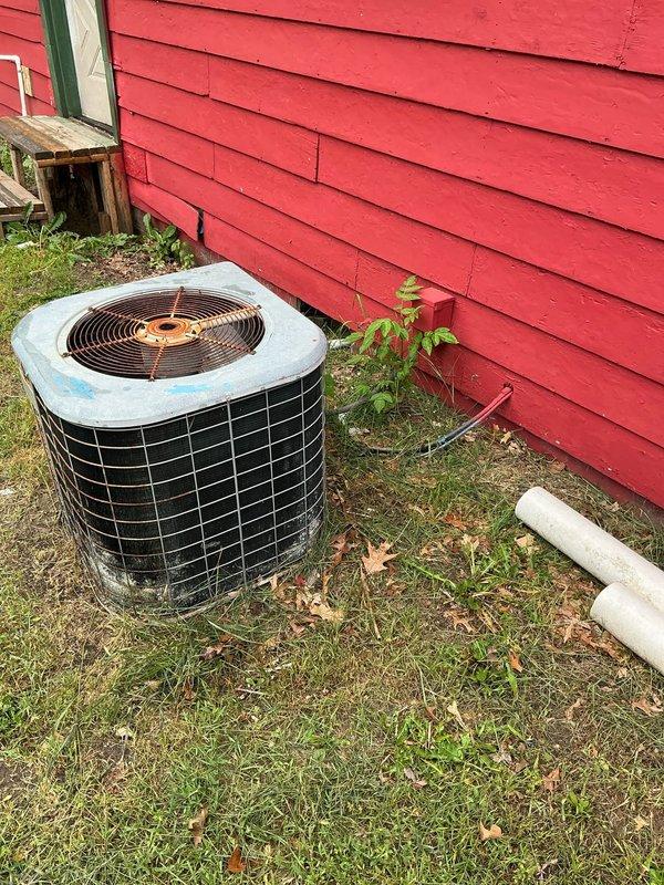 Performed comprehensive assessment of outdoor air conditioning condenser unit showing significant age-related wear, weathering, and deterioration. Unit exhibits rust spots, discoloration, and accumulated debris, with installation positioned against building exterior on uneven ground surface. Documented current equipment condition through photographic evidence and provided estimate for AC system evaluation and potential replacement or repair recommendations.