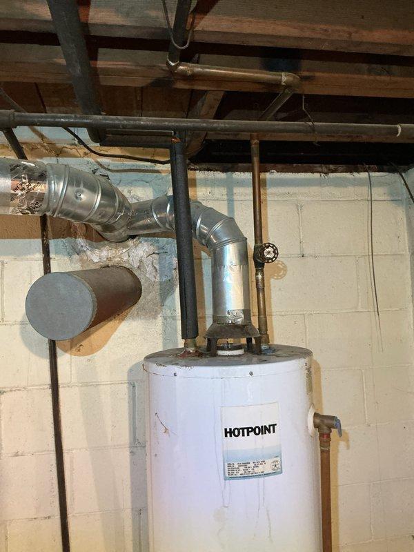Responded to emergency water heater leak at residential property. Upon arrival, inspected 10-year-old Hotpoint water heater located in basement utility area. Identified active leak originating from water heater tank. Documented existing installation including venting system with metal flue pipe properly connected through ceiling structure and aluminum flexible ductwork. Assessed condition of unit and surrounding infrastructure, noting age of equipment and deterioration of materials in mechanical space. Photographed water heater installation, venting configuration, and overall system setup for service records. Provided customer with assessment findings and recommendations for water heater replacement due to age and tank failure.