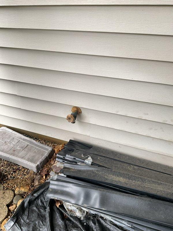 Responded to active water leak emergency where main water supply to home had been shut off to prevent further damage. Upon inspection, identified outdoor hose bib (spigot) line as source of leak penetrating into home. Documented existing conditions showing exterior brass spigot mounted on white vinyl siding with visible foundation deterioration and water damage at base of wall. Water infiltration had compromised foundation area where spigot line enters structure. Photographed affected areas including damaged foundation components, black waterproofing membrane exposure, and debris accumulation indicating ongoing moisture issues. Main water supply remained in shut-off position to protect property until permanent repairs could be completed.