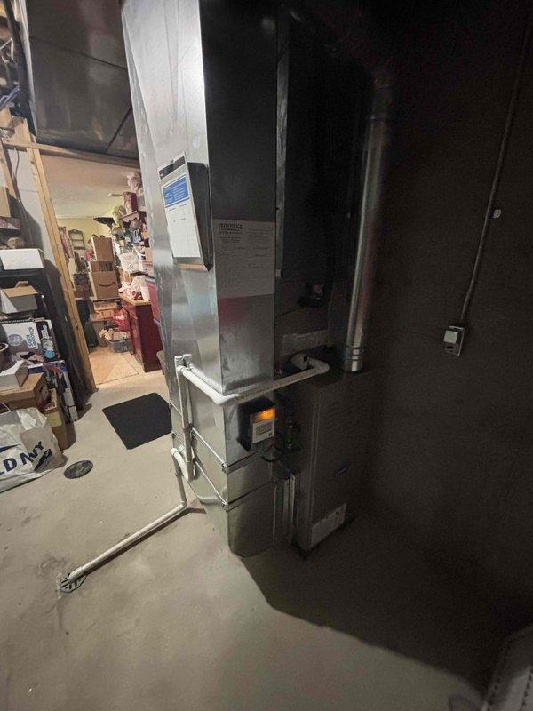 Completed full HVAC system installation in residential basement utility area. Installed new furnace unit with integrated control panel and digital display, connected to white-painted supply ductwork extending vertically and horizontally throughout the space. Configured all ductwork connections including rectangular trunk line and cylindrical branch ducts to ensure proper airflow distribution. Positioned equipment on concrete pad in mechanical room, verified all electrical connections to panel, and confirmed proper venting. System tested and operational upon completion with all manufacturer specifications met.